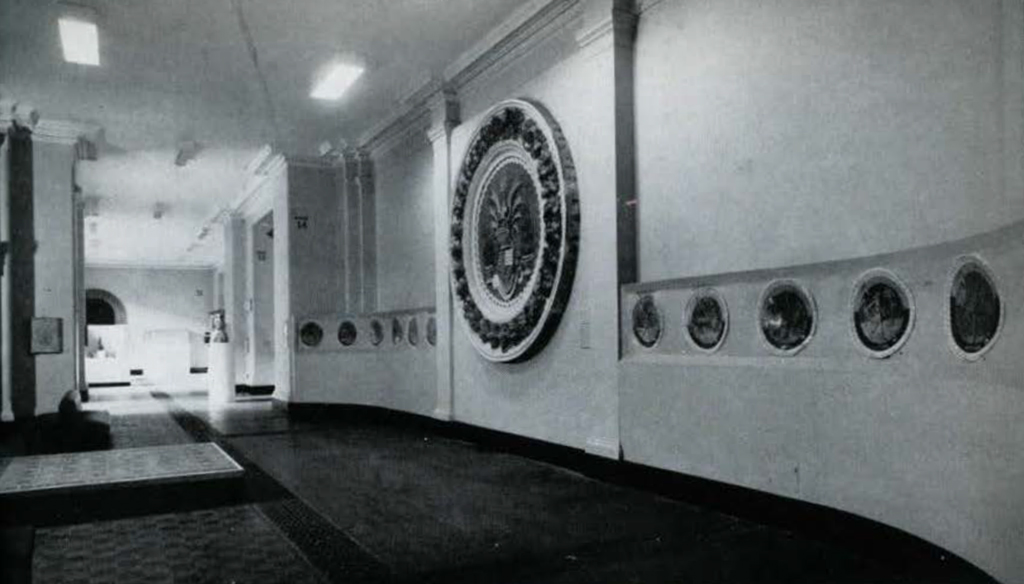 A gallery hallway with a large seal on the wall.