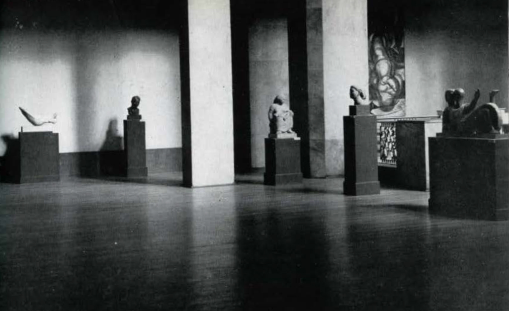 A largely empty gallery with small sculptures on pedestals.