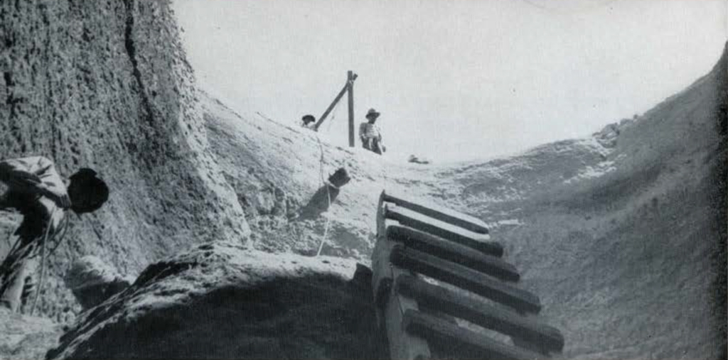 Looking up from a cylindrical pit to the surface, men standing above, and a ladder reaching up.