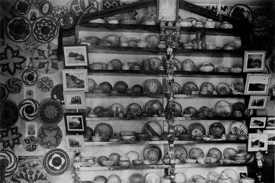 A large bookcase with shelves filled of Hopi pottery, the walls around the bookcase adorned with woven basekts.