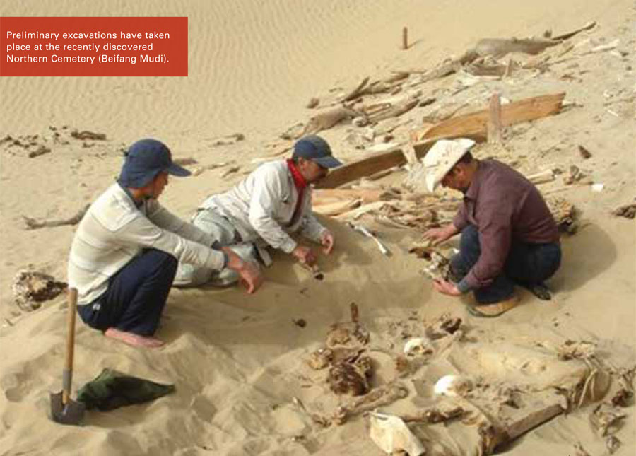 Three people excavating a cemetery in the sand, debris litered about them.