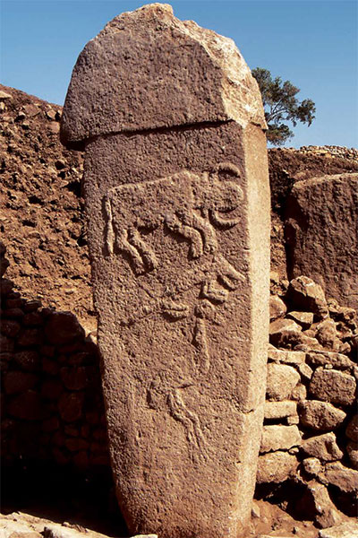 A stone pillar with a horned cow, a fox, and a bird carved into it.