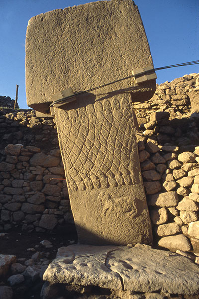 A massive stone pillar with a band of snake carvings forming a net pattern.