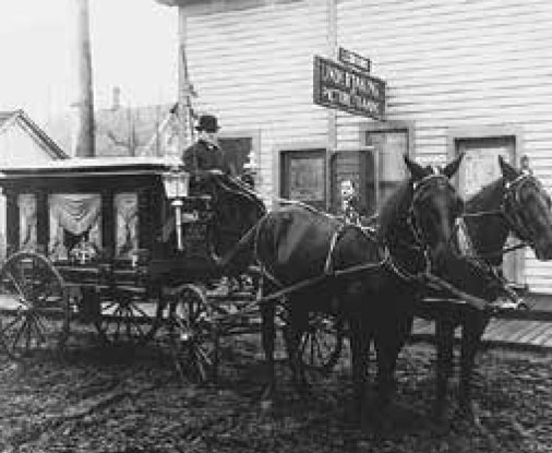 A horse drawn hearse outside an old building.