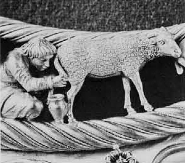 Close up of a depiction of a person kneeling and milking a sheep, found on a gold necklace.