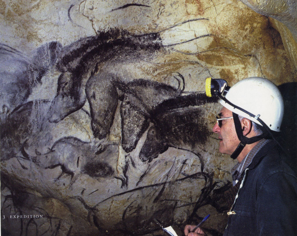 Jean Clottes wearing a helmet with headlamp next to cave paintings of horses and boars.