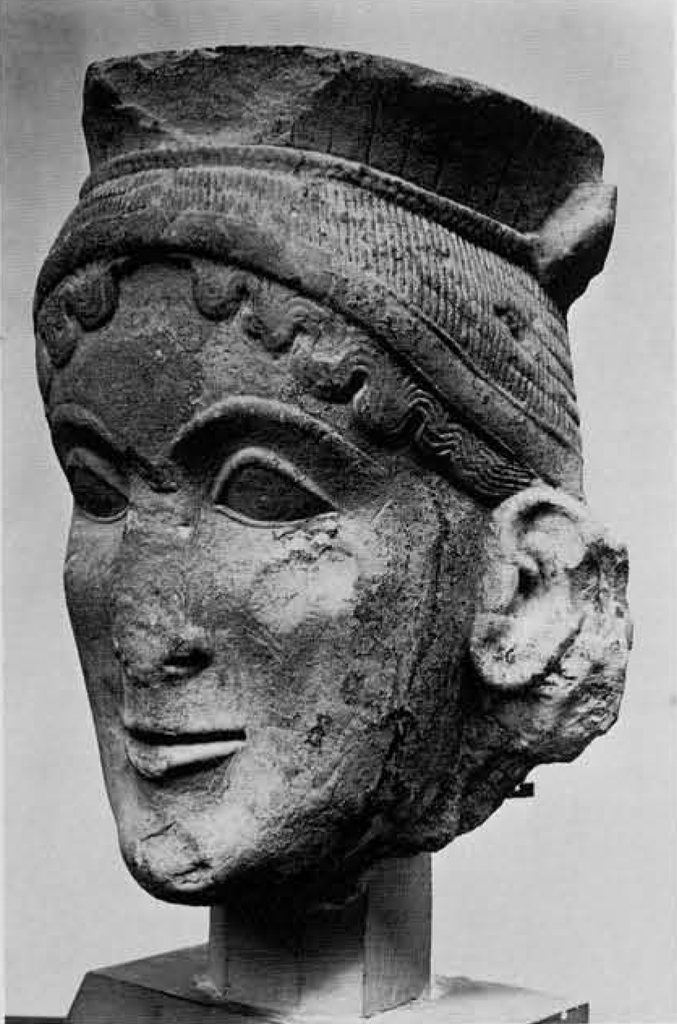 Large limestone head of a female with hair peaking out from under a hat.