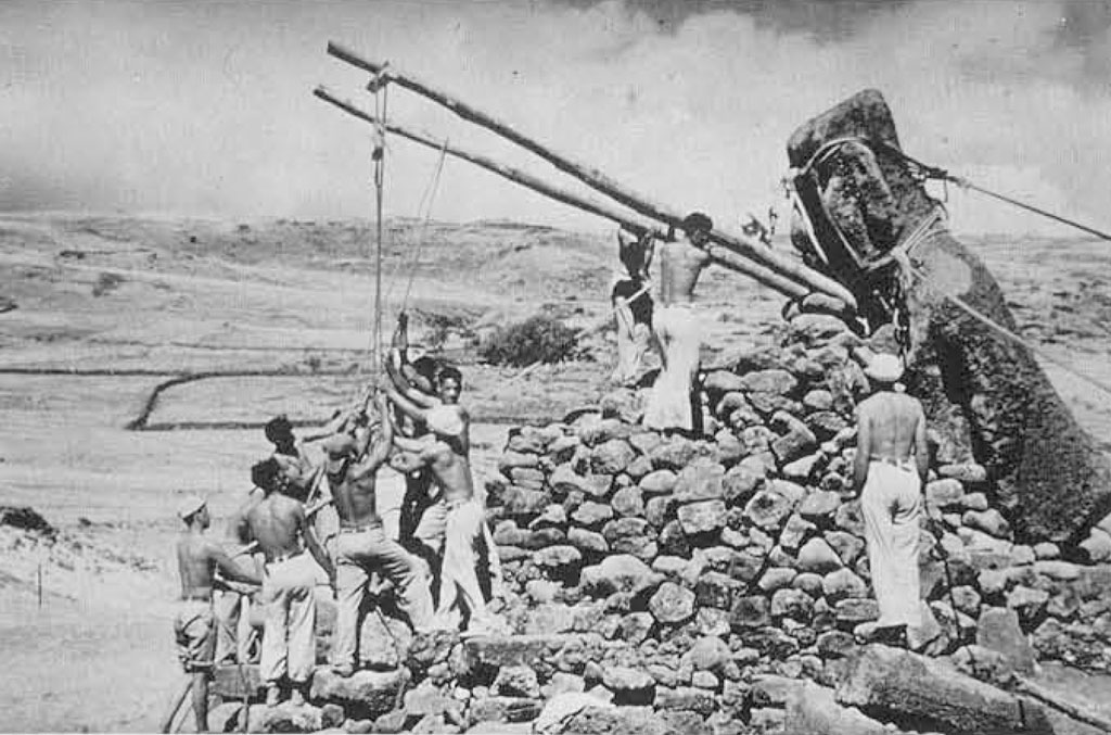 A group of men levering a massive stone statue upright using ropes and poles.