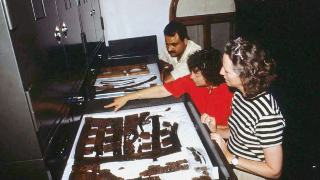 Three people examining furniture fragments laid out in large, flat drawers.