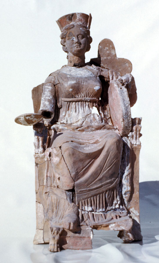 A stone statue of a seated person in draped clothing, wearing a headpiece.