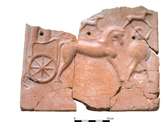 A terracotta tile, pieced back together from fragments, showing a horse and chariot, and a warrior holding a shield in front.