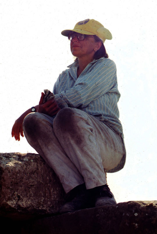 A woman in a yellow hat, crouching near a stone at Gordion.