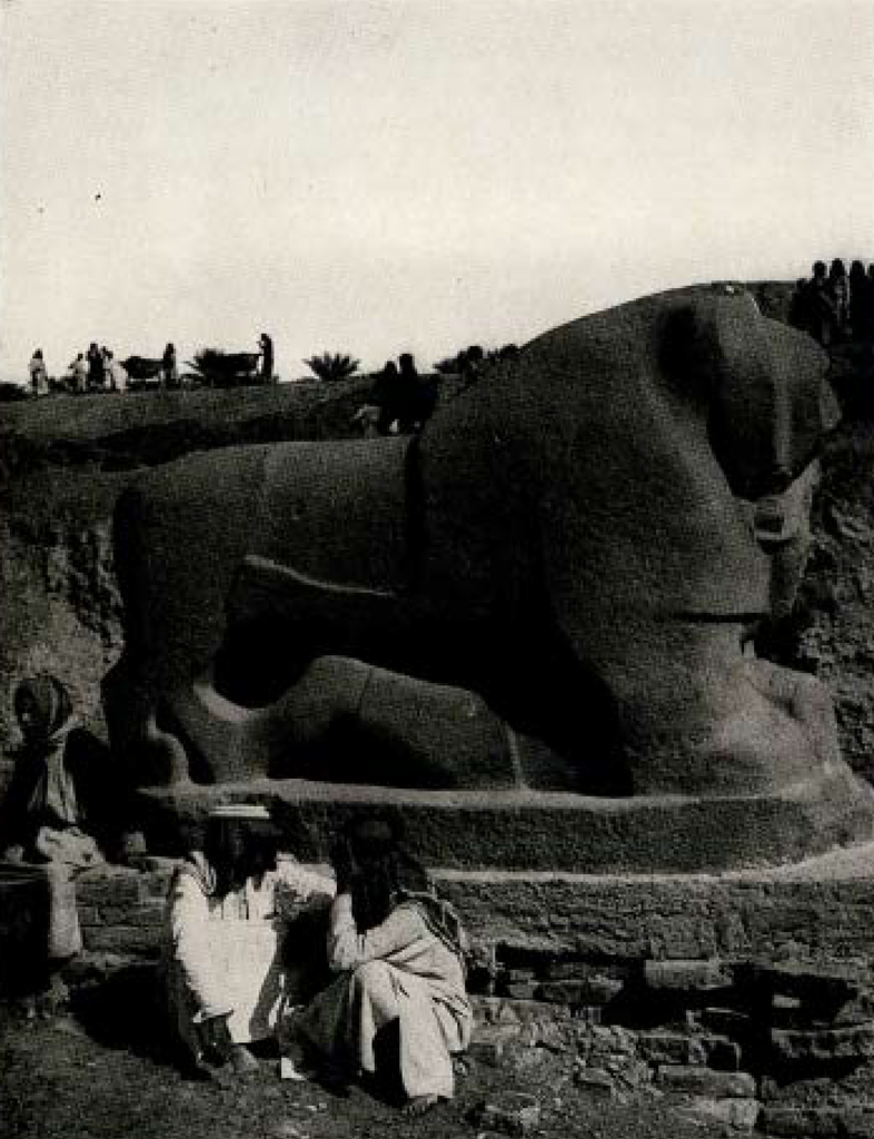 Two men crouching next to a massive lion statue