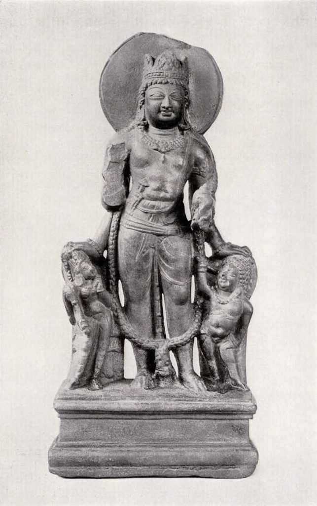 statue of Vishnu wearing crown with round halo standing between two much smaller attendants, his left hand resting on the left attendant's head