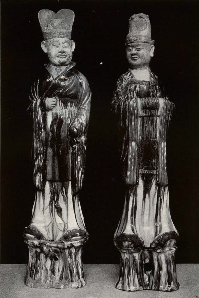 Two robed official figures, left with two humped headdress and one arm at his side and one arm across his waist, right with round headdress and hands clasped at the waist obscured by long sleeves
