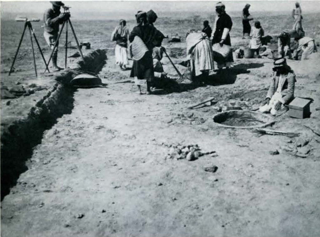 People excavating, one man kneeling at a circular pipe