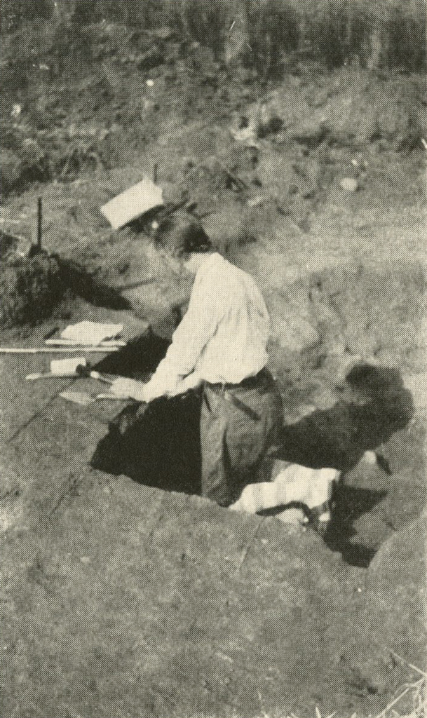 A person standing waist deep in a pit with a set of tools in front of them