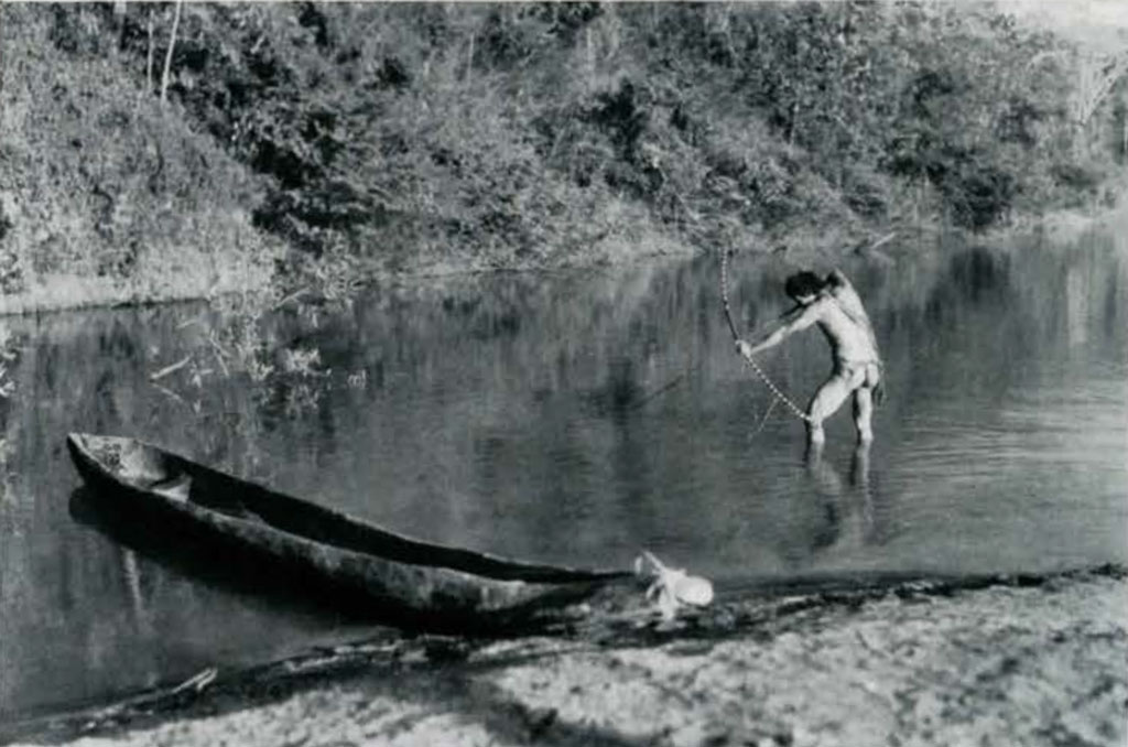A man standing in a river at calf height with bow drawn aimed at the water
