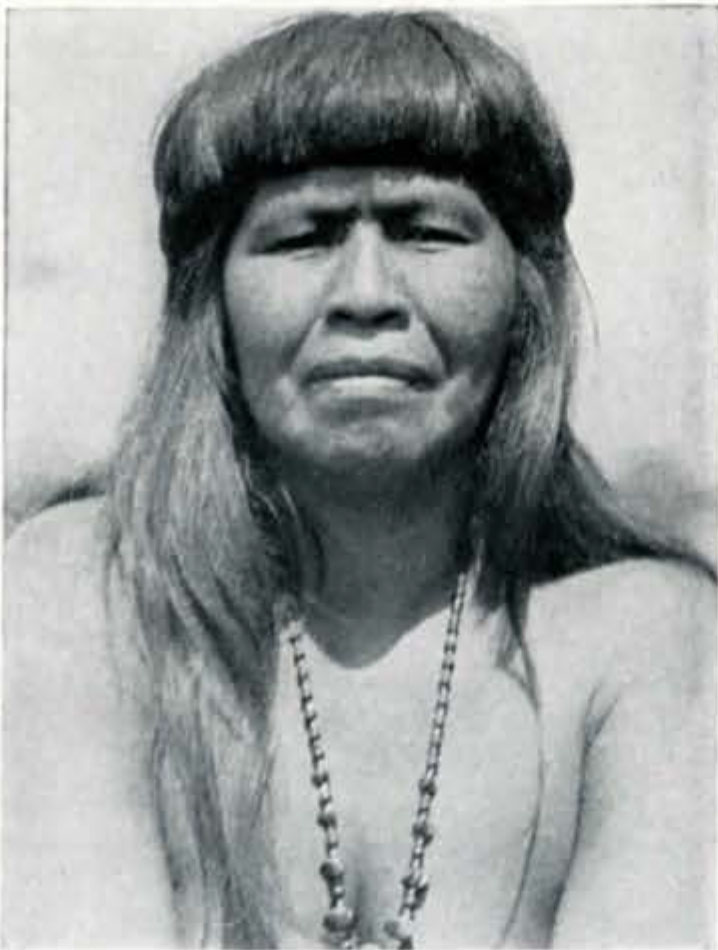 Portrait of a woman with long hair and bangs, wearing a beaded necklace