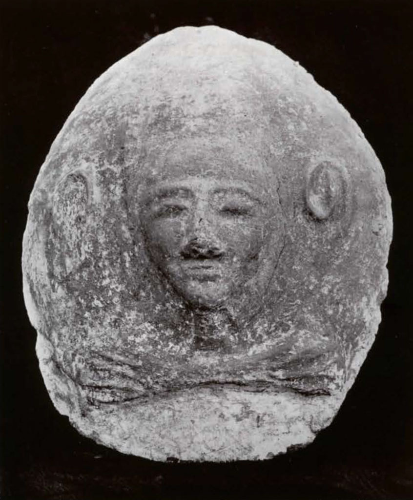 Sarcophagus oval lid showing a face and ears with crossed hands