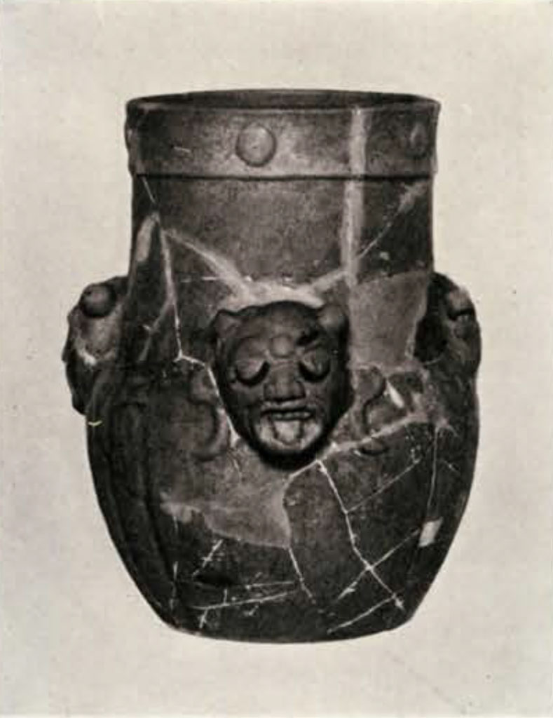 A fragmented vase pieced back together with three faces in relief with tongues out